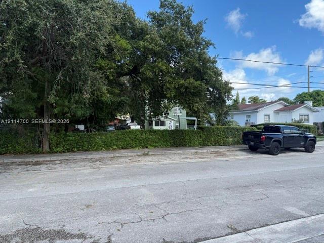 Mature tree canopy, manicured privacy hedge, and paved street access