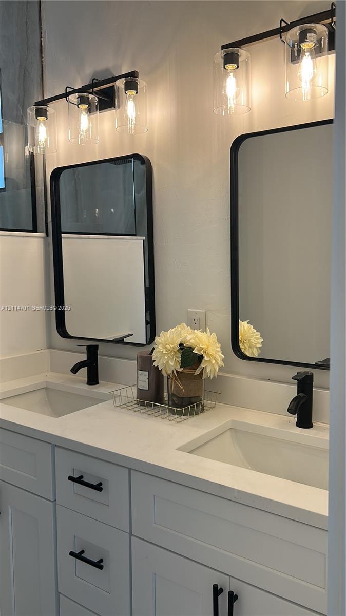 Double vanity featuring shaker-style cabinetry, rectangular undermount sinks, stone-finish countertops, matte black faucets, and matching black-framed mirrors