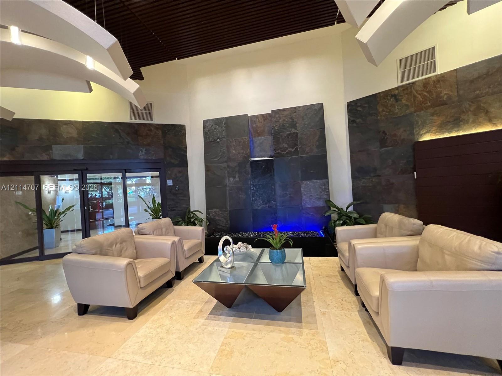 Lobby area featuring tile flooring, stone-clad accent walls, a built-in water feature, and a vaulted ceiling with architectural lighting