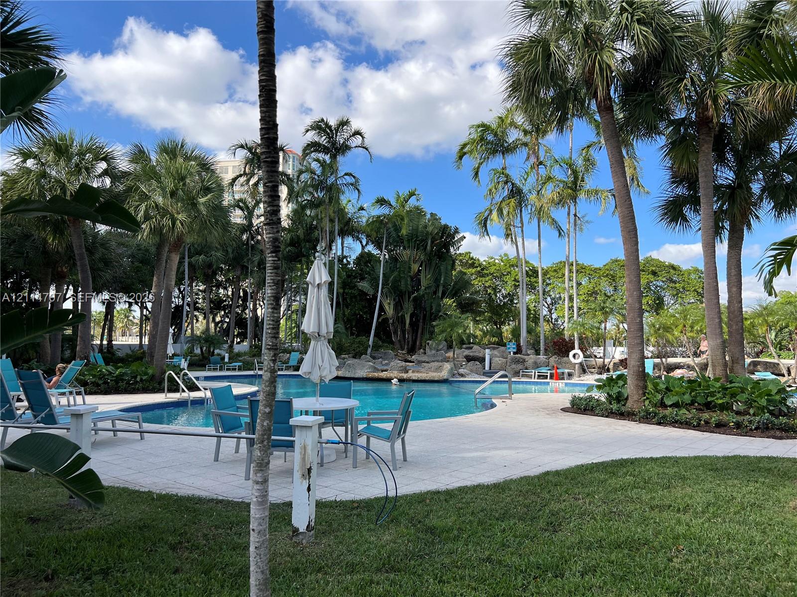 Swimming pool with stone rock feature, paver deck, and mature palm trees