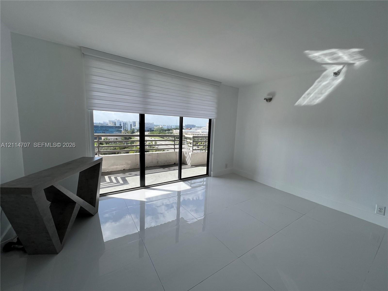 Large-format tile flooring, wall-mounted lighting fixture, floor-to-ceiling sliding glass doors, and a private balcony with metal railing