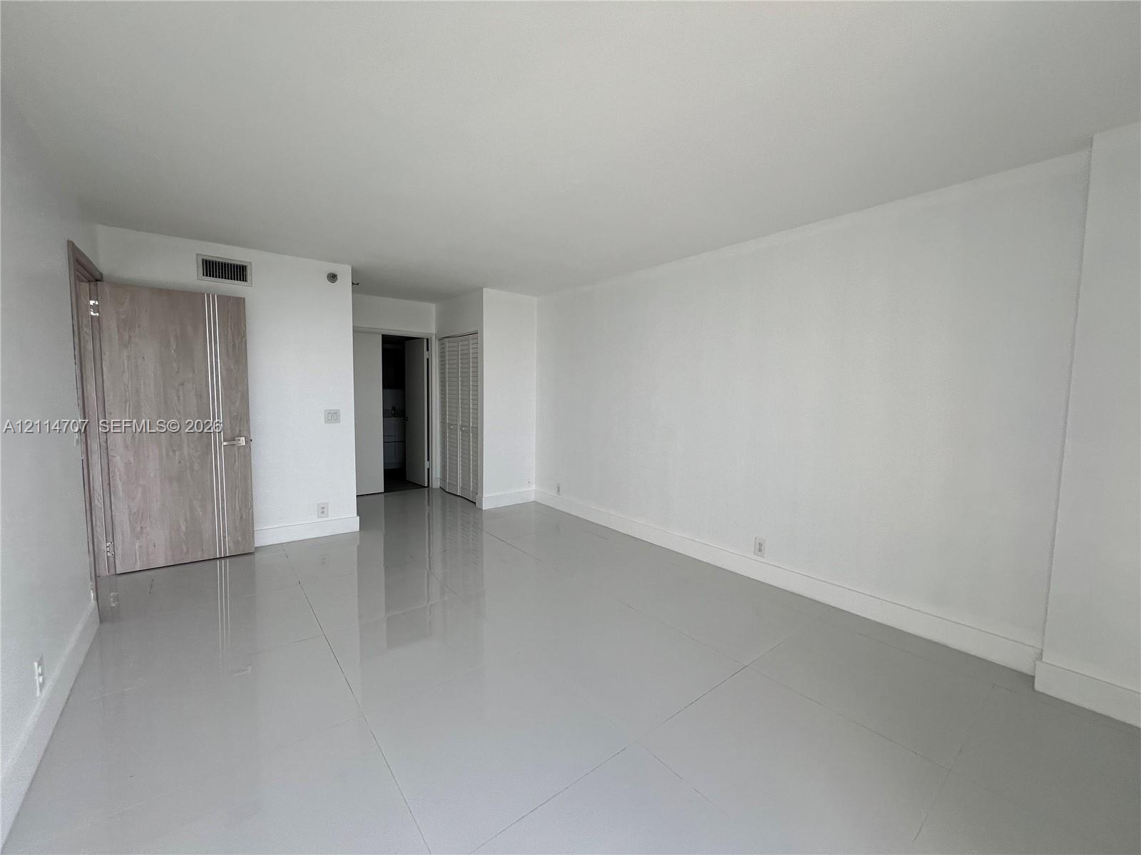 Open living area featuring large-format polished tile flooring, neutral wall finishes, a solid-core door with vertical detailing, and louvered closet doors