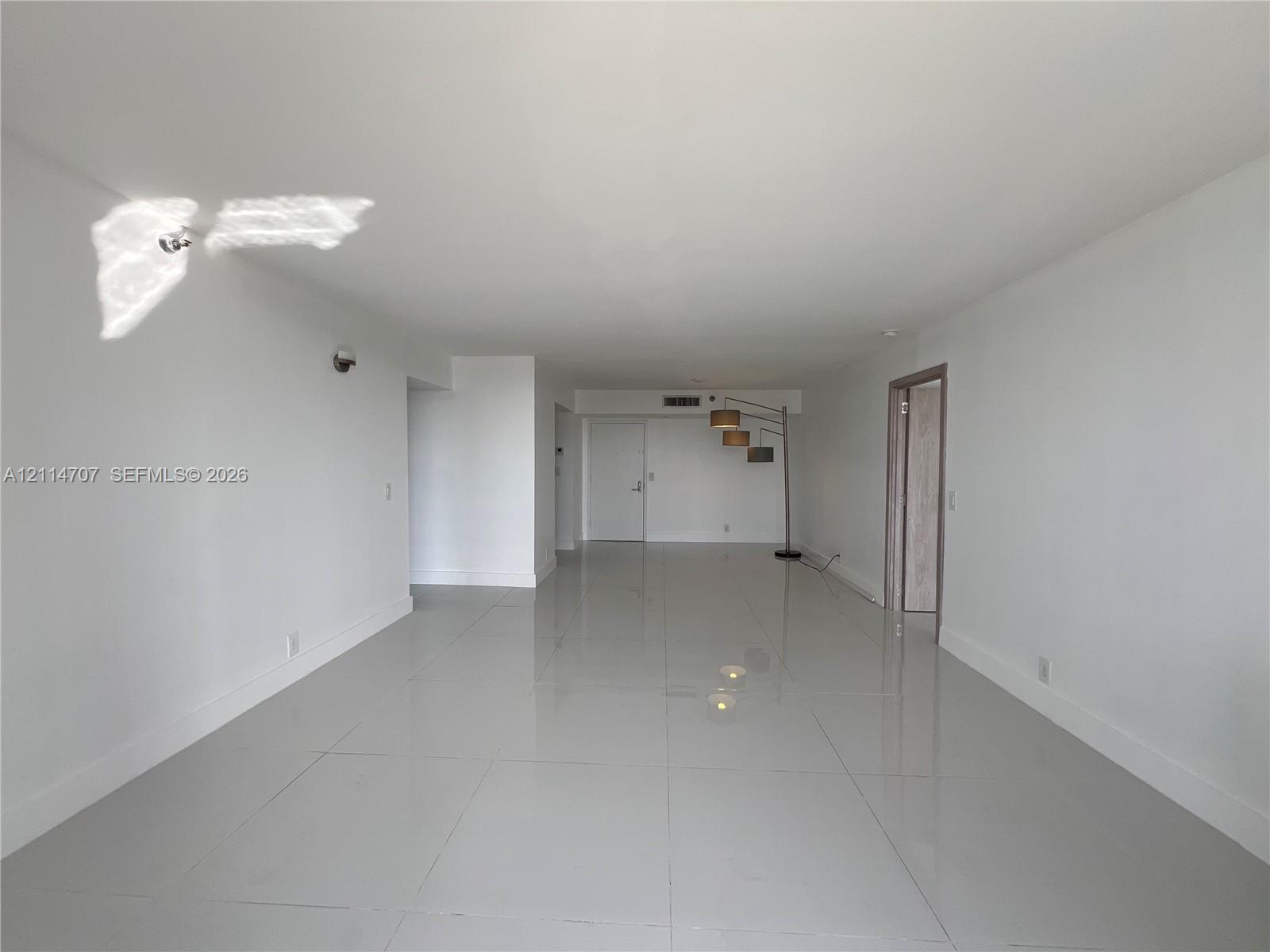 Open-concept interior space featuring high-gloss tile flooring, smooth ceilings, and interior door frames with a natural wood finish