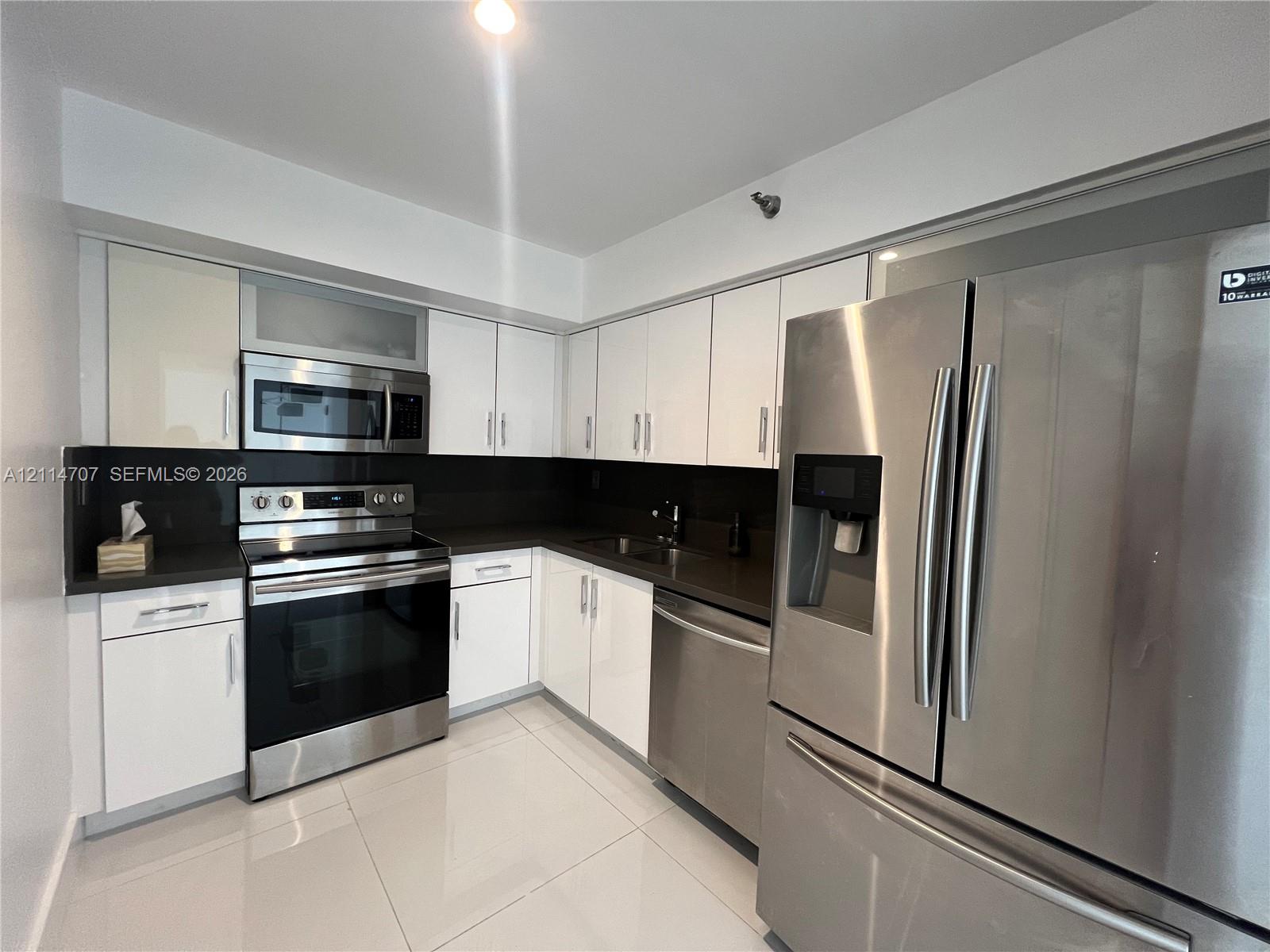 Kitchen featuring white high-gloss cabinetry, dark solid-surface countertops, stainless steel appliances, and large-format tile flooring