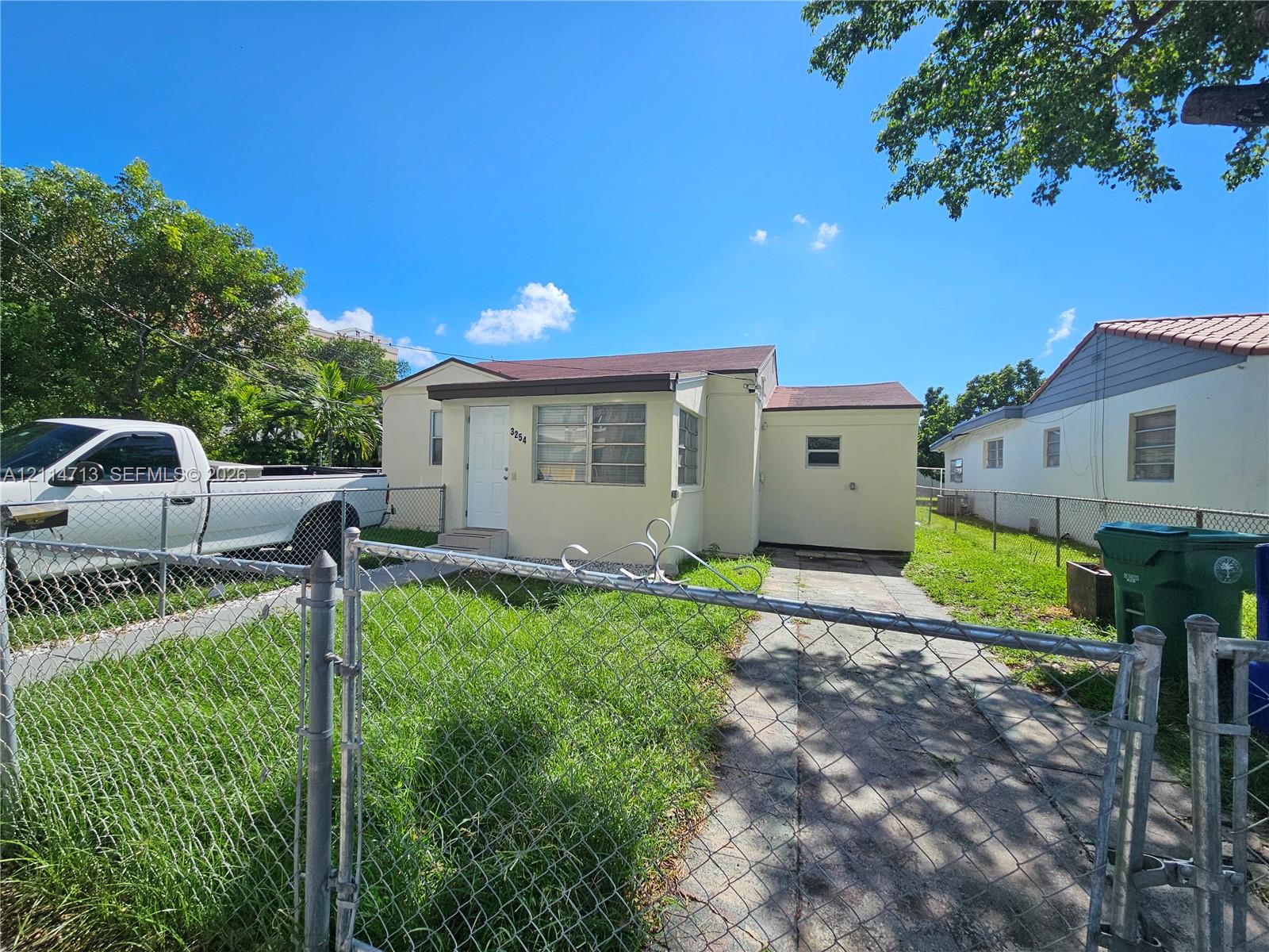 Single-story exterior featuring a light-toned stucco facade, a concrete driveway, and a chain-link fenced perimeter