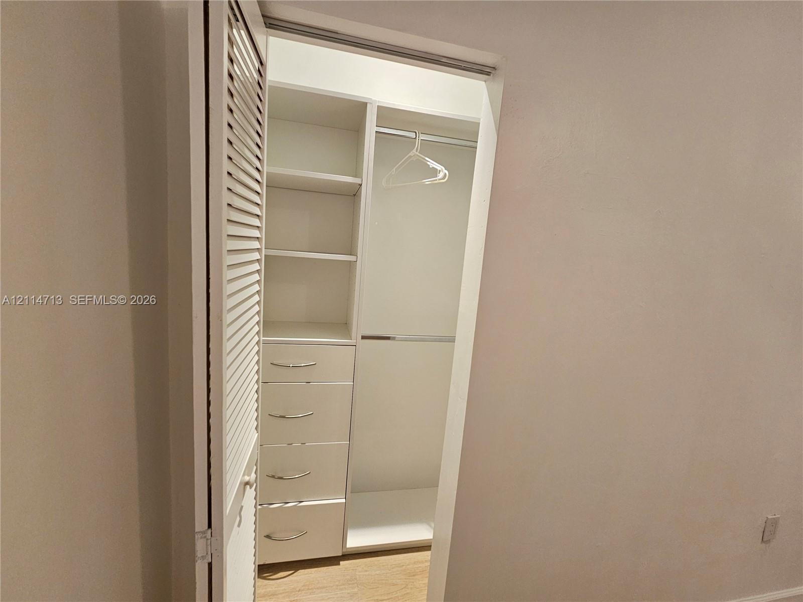 Closet featuring custom white built-in shelving, a series of four integrated drawers, a metal hanging rod, and a louvered door