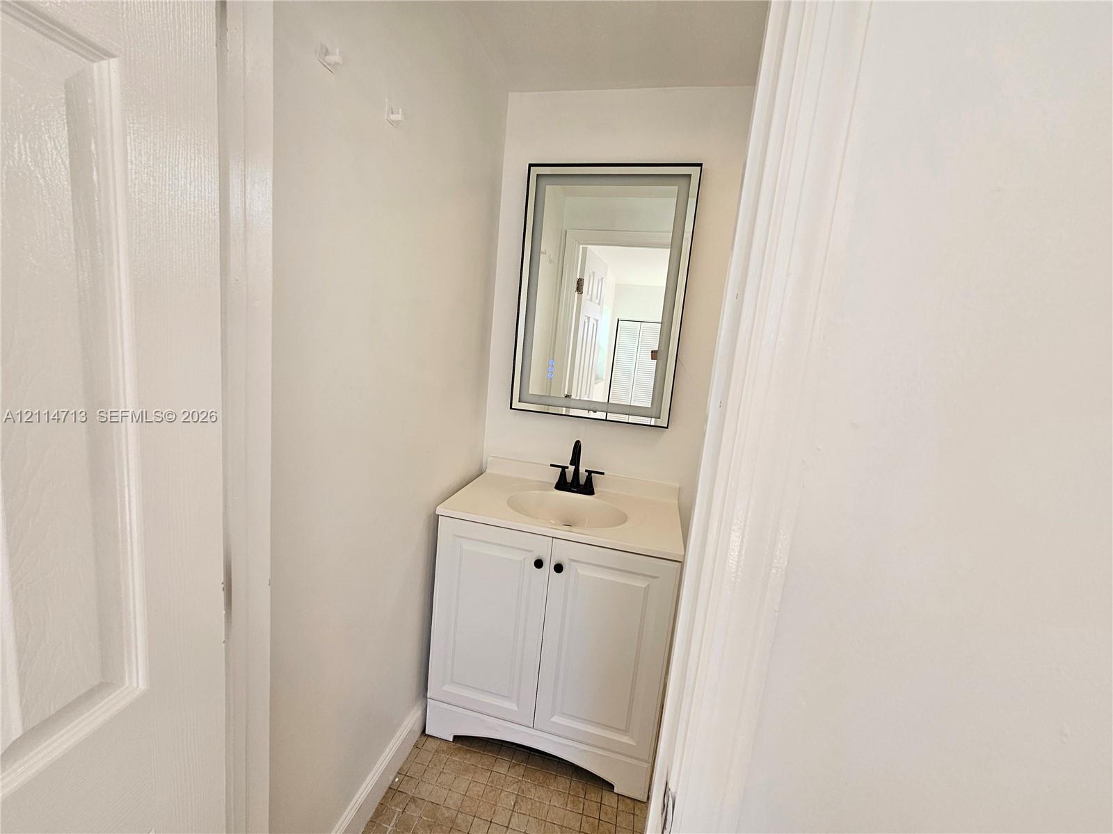 White vanity cabinet featuring an integrated sink, stone-finish countertop, matte black faucet, and a rectangular mirror