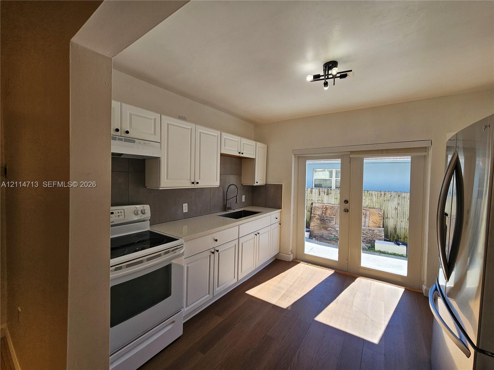 Kitchen featuring white shaker-style cabinetry, quartz countertops, tile backsplash, wood-finish flooring, and glass-paned sliding doors