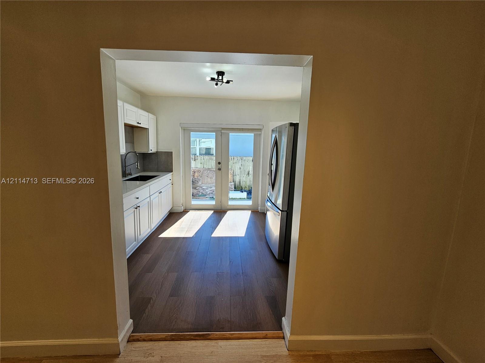 Kitchen featuring white cabinetry, wood-finish flooring, stainless steel refrigerator, and glass-paneled double doors