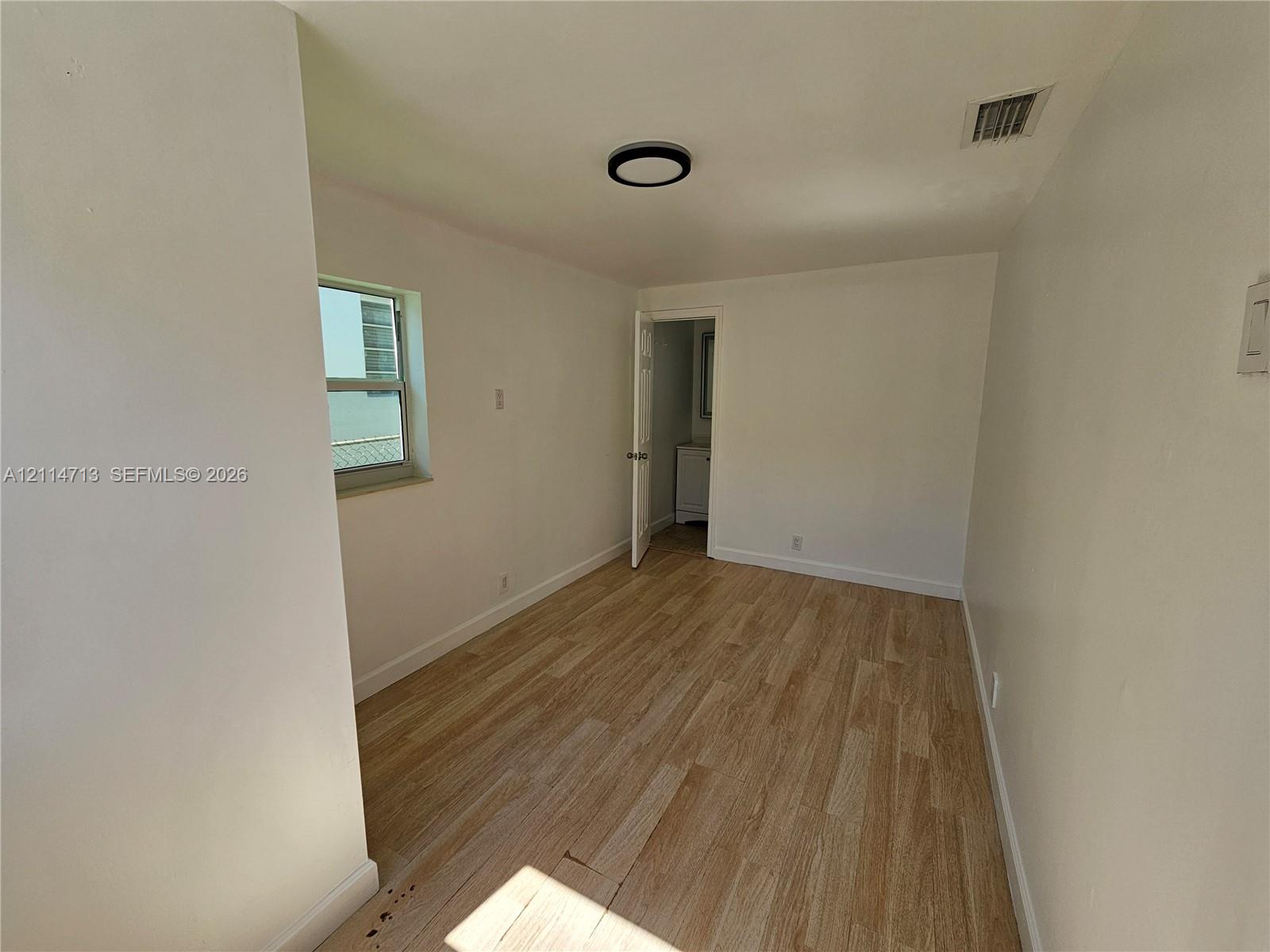 Room featuring wood-finish flooring, a single-pane window, and a modern circular flush-mount ceiling light fixture