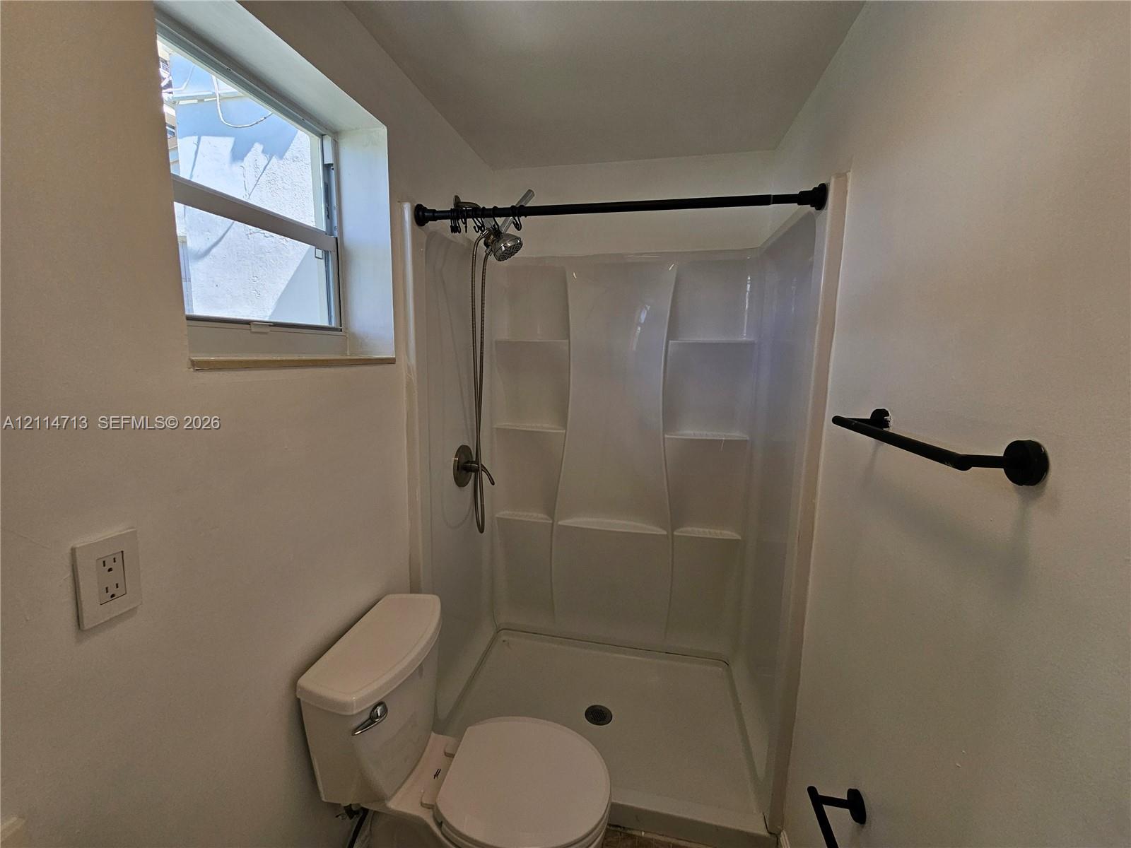Shower stall featuring a molded surround with integrated shelving, matte black fixtures, a single-hung window, and a wall-mounted towel bar