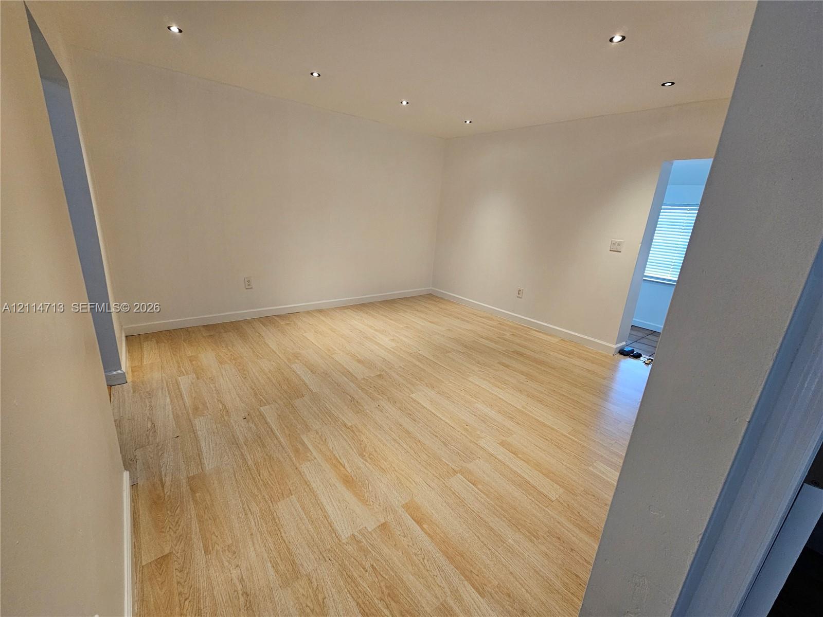 Open-concept interior space featuring light-toned wood-finish flooring, neutral wall tones, and recessed ceiling lighting