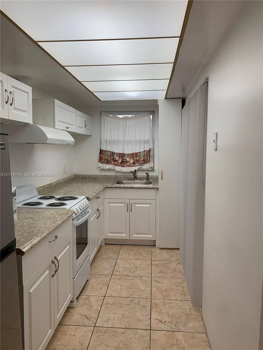 Kitchen featuring white cabinetry, stone-finish countertops, tile flooring, integrated ceiling panel lighting, and a metal sink with a faucet
