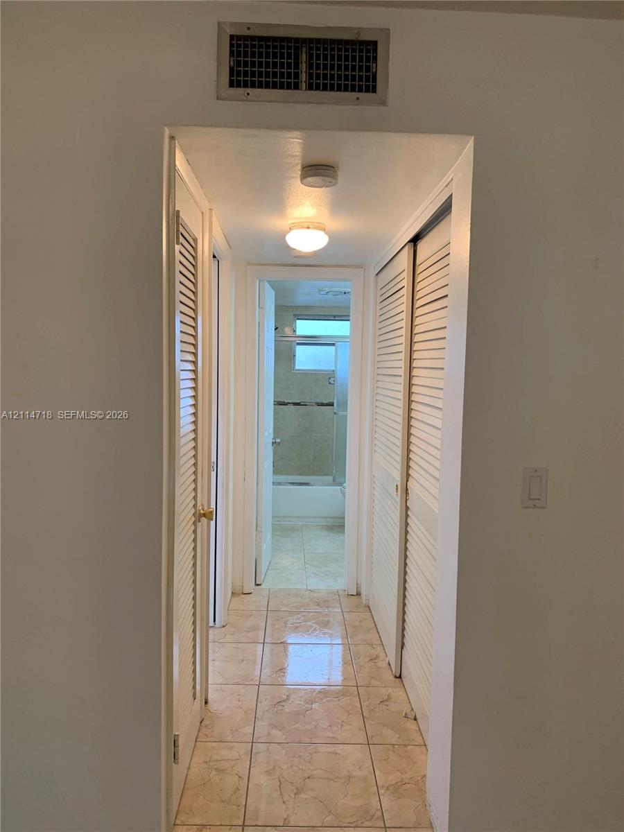 Hallway featuring floor-to-ceiling louvered closet doors, polished tile flooring, and flush-mount lighting