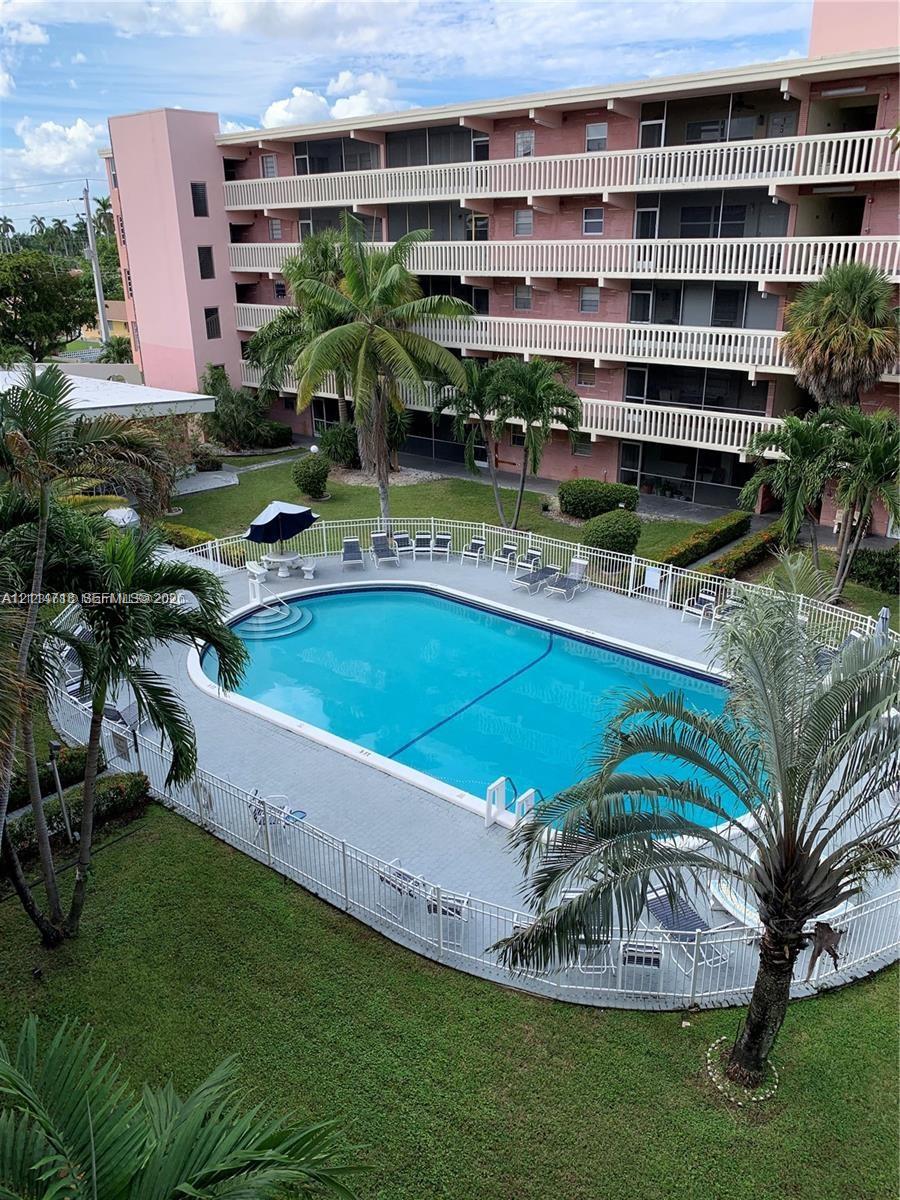 In-ground swimming pool with perimeter fencing, paved deck, manicured green space, mature palm trees, and multi-story building exterior In-ground swimming pool with perimeter fencing, paved deck, manicured green space, mature palm trees, and multi-story building exterior