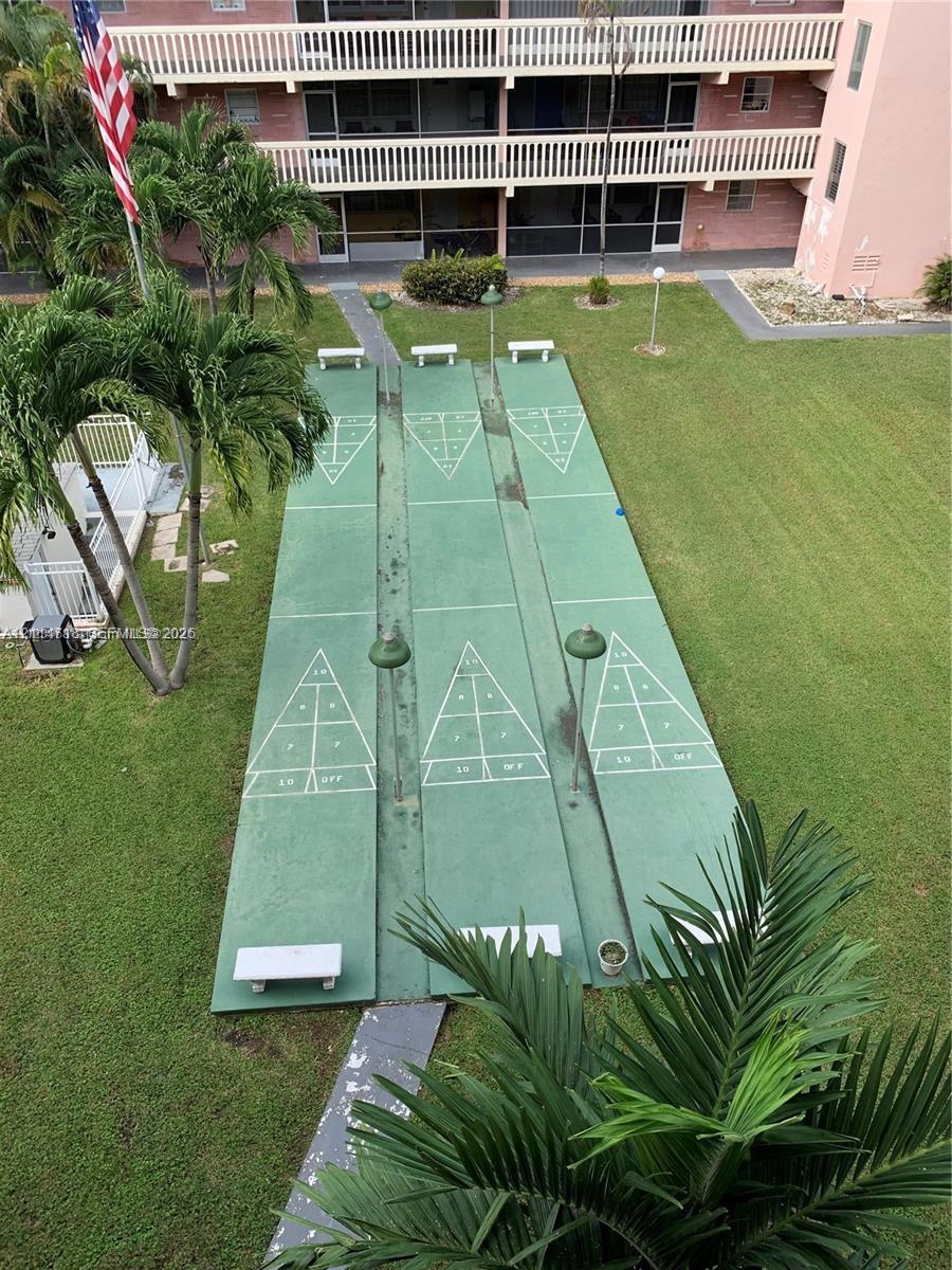 Common recreation area featuring three painted shuffleboard courts, built-in benches, pole-mounted lighting, and landscaped grounds