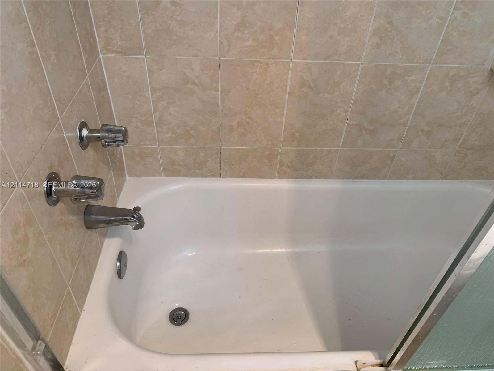 Bathtub featuring a white basin, neutral-toned square wall tiling, and chrome metal faucet hardware