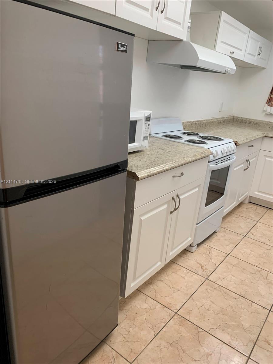 White cabinetry, stone-finish countertops, tile flooring, stainless steel refrigerator, and white electric range with hood