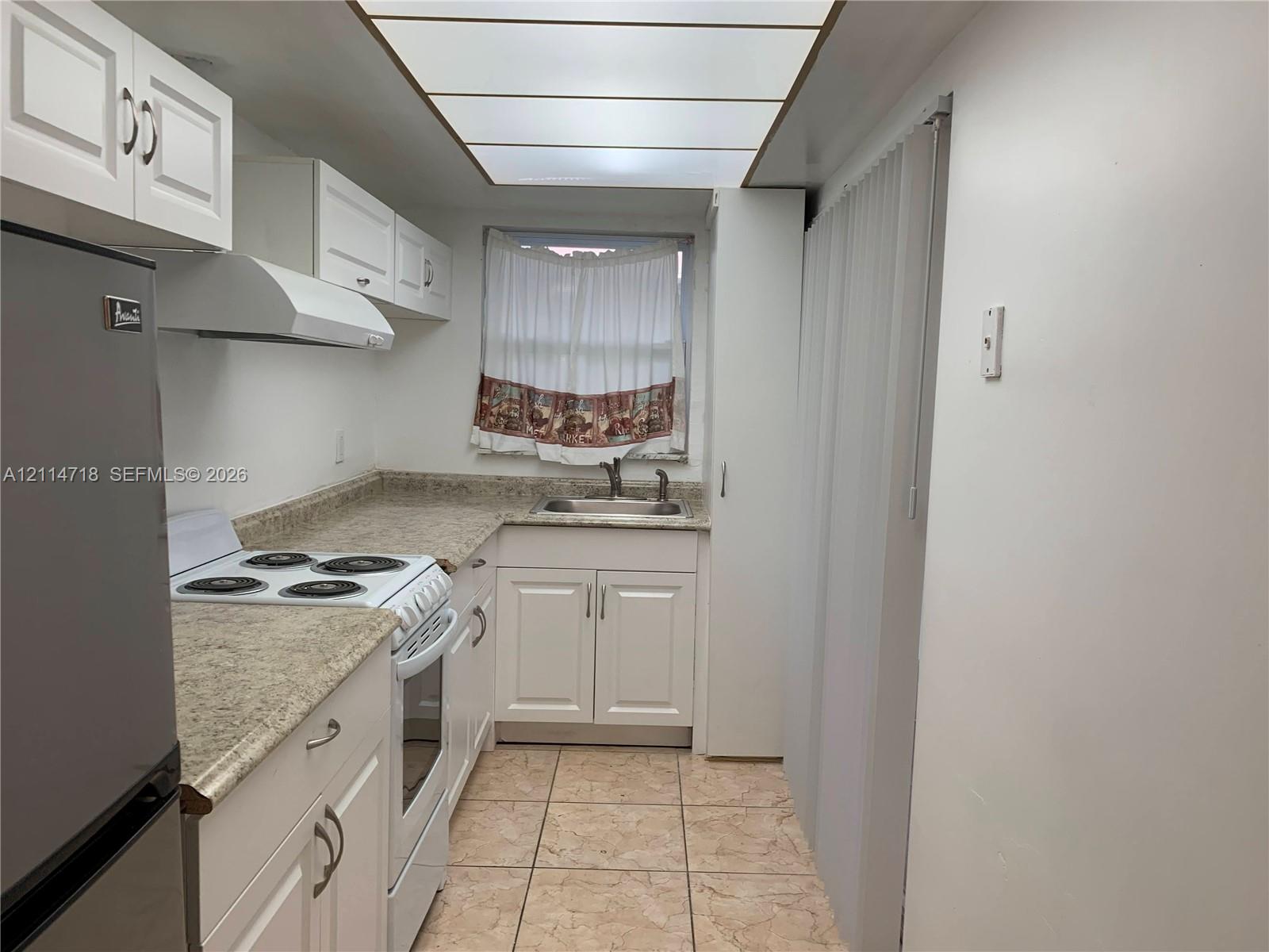Kitchen featuring white shaker-style cabinetry, stone-finish countertops, tiled flooring, integrated drop-ceiling lighting, and a double-basin stainless steel sink