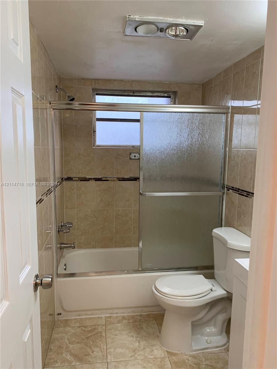 Bathroom featuring floor-to-ceiling tile surround with decorative accent inlay, sliding glass shower door, tub-shower combination, and tiled flooring