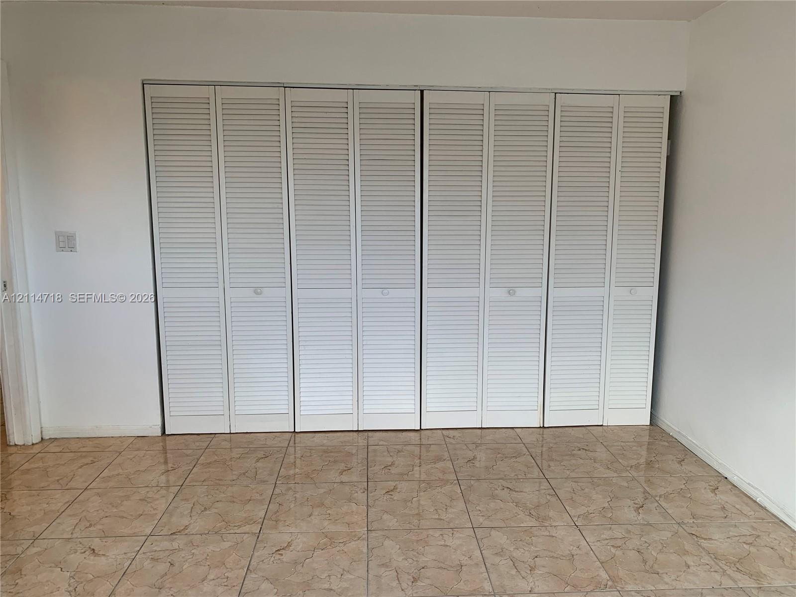 Wall-to-wall folding louvered closet doors and neutral tile flooring