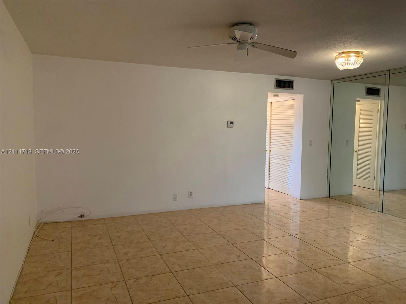 Neutral tile flooring, mirrored wall paneling, ceiling fan with light fixture, flush-mount decorative ceiling light, and louvered closet doors