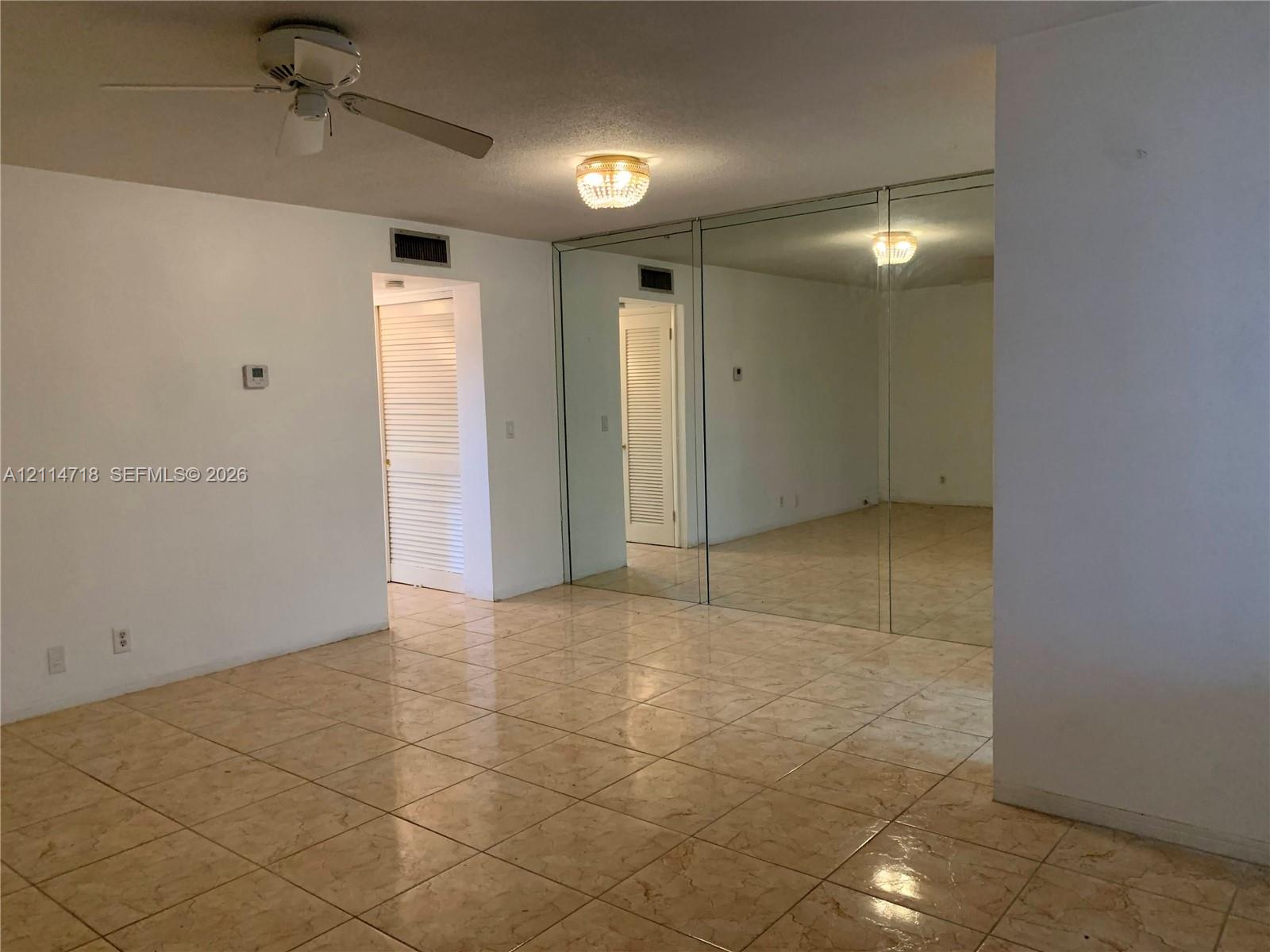 Ceramic tile flooring, full-wall mirrored closet doors, ceiling fan with light kit, and flush-mount ceiling fixture