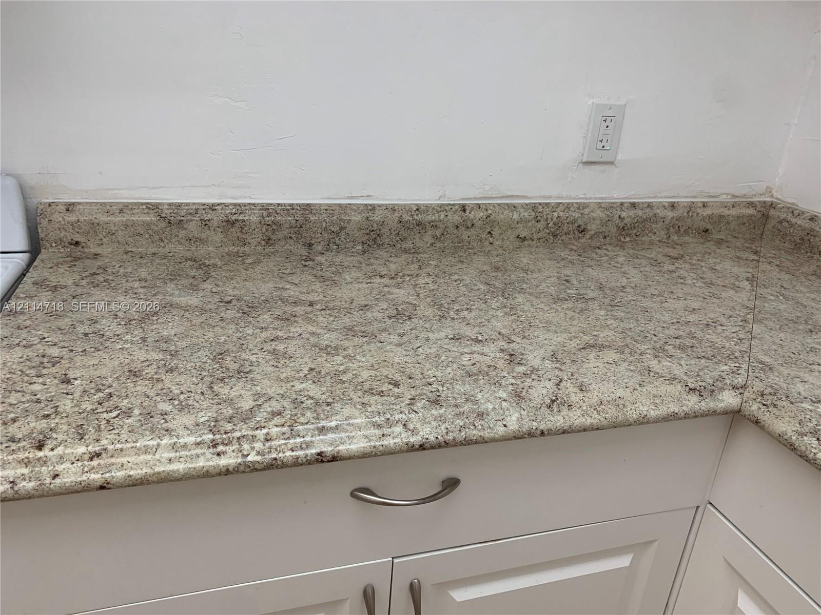 Speckled stone-finish countertop with integrated backsplash and white cabinetry featuring brushed metal pulls