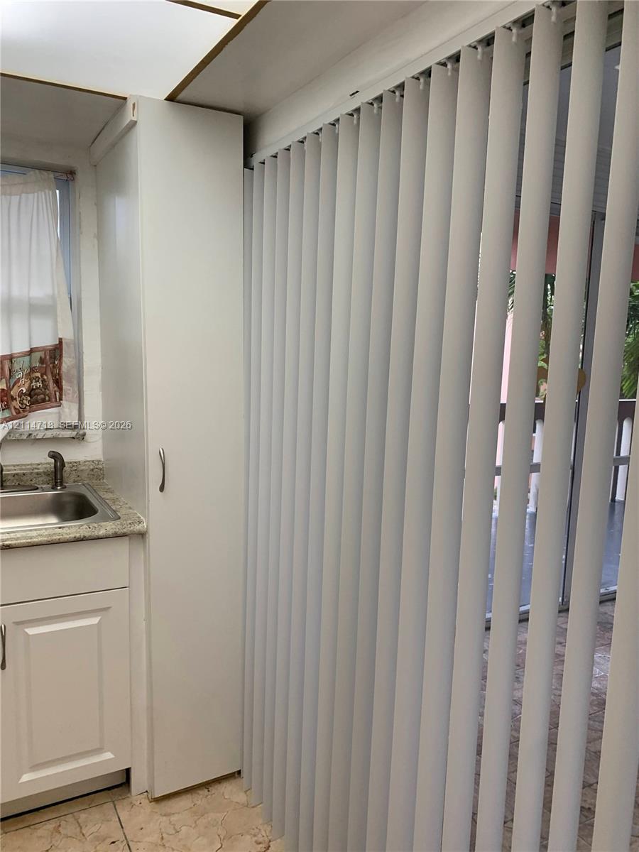 Built-in floor-to-ceiling cabinetry, stone-finish countertop, undermount stainless steel sink with metal faucet, and floor-to-ceiling vertical blinds