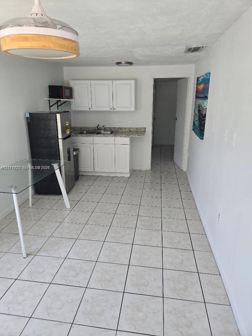 Kitchenette featuring white cabinetry, stone-finish countertops, ceramic tile flooring, and a pendant ceiling light fixture