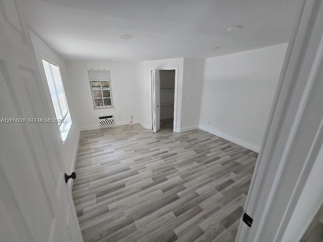 Interior room featuring wood-finish flooring, recessed ceiling lighting, a dedicated closet with built-in shelving, and a wall-mounted air conditioning unit