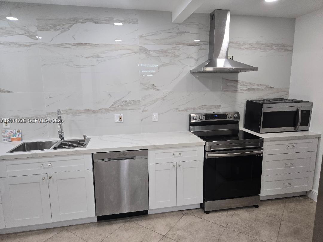 Kitchen featuring white cabinetry, large-format stone-patterned tile backsplash, stainless steel appliances, and solid surface countertops Kitchen featuring white cabinetry, large-format stone-patterned tile backsplash, stainless steel appliances, and solid surface countertops