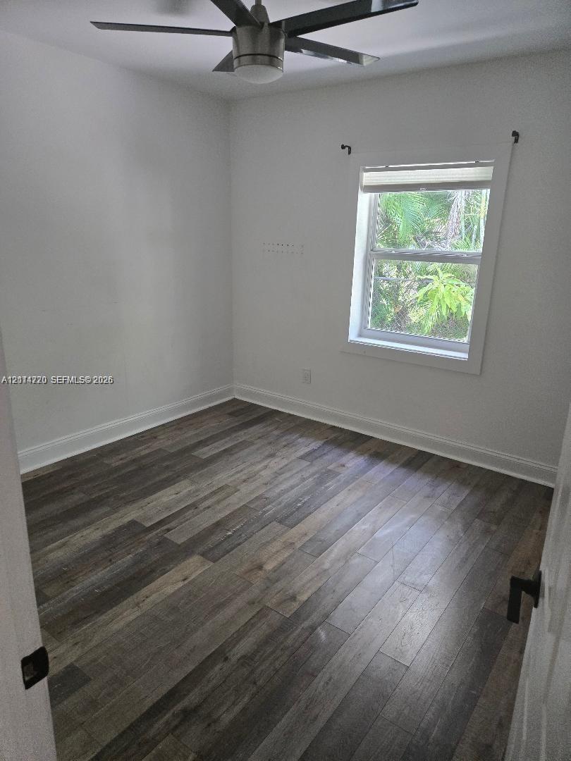 Wood-finish flooring, multi-blade ceiling fan with central light fixture, and single-pane window with white trim