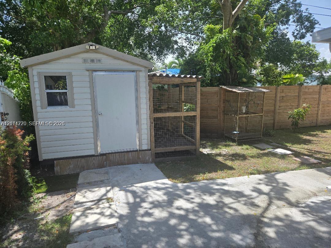 Outdoor storage shed featuring horizontal siding, a single-entry door, and an attached wire-mesh enclosure, set within a fenced perimeter