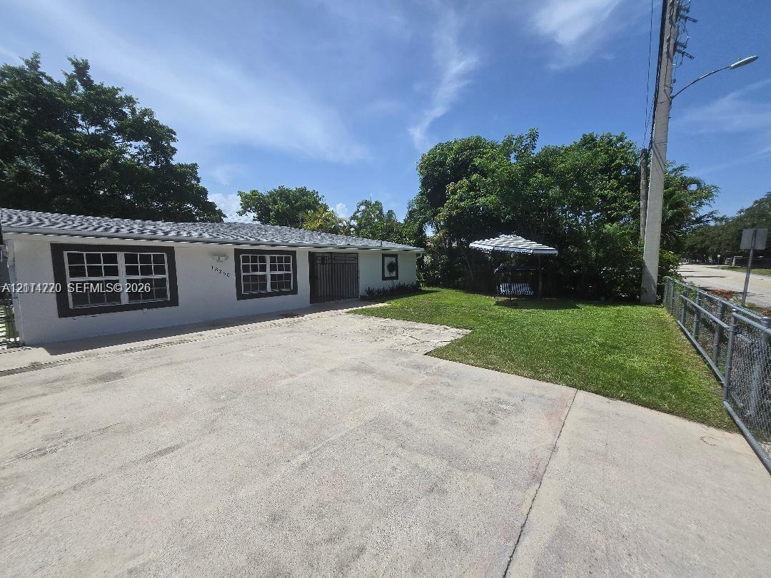 Single-story residence featuring a concrete driveway, grid-pattern windows, a hip roof, and a lawn enclosed by chain-link fencing Single-story residence featuring a concrete driveway, grid-pattern windows, a hip roof, and a lawn enclosed by chain-link fencing