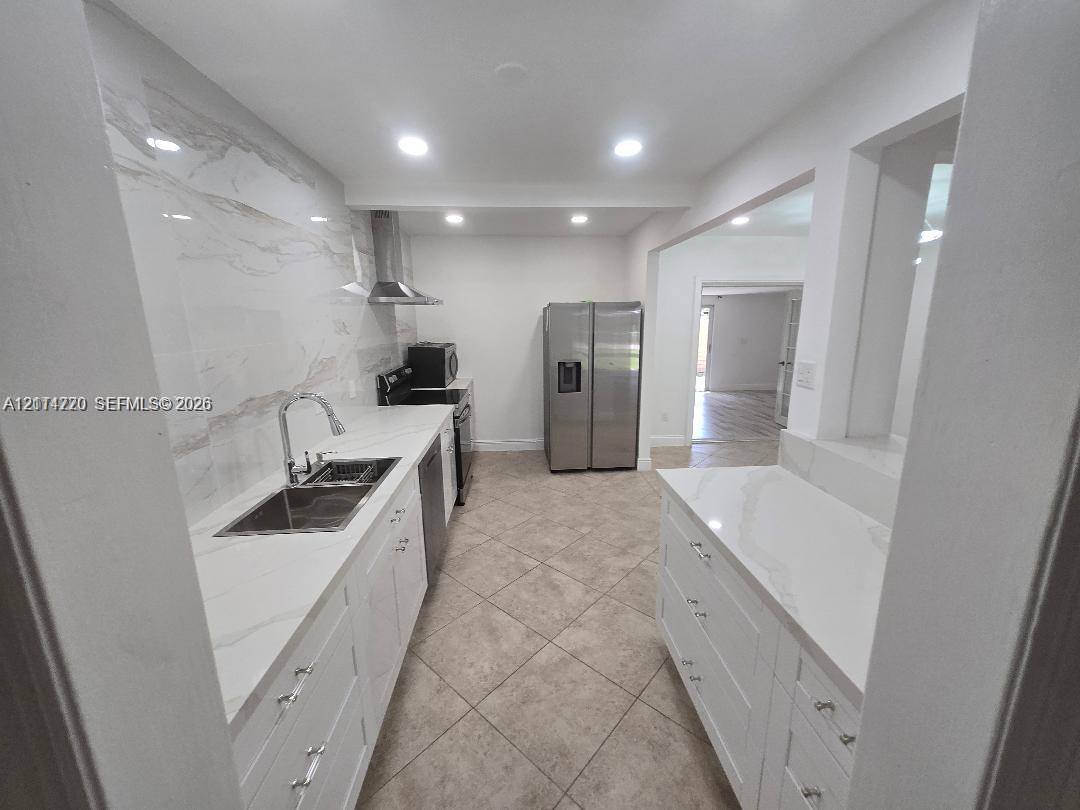 Kitchen featuring white shaker-style cabinetry, quartz countertops, full-height stone-look backsplash, stainless steel appliances, and tile flooring Kitchen featuring white shaker-style cabinetry, quartz countertops, full-height stone-look backsplash, stainless steel appliances, and tile flooring