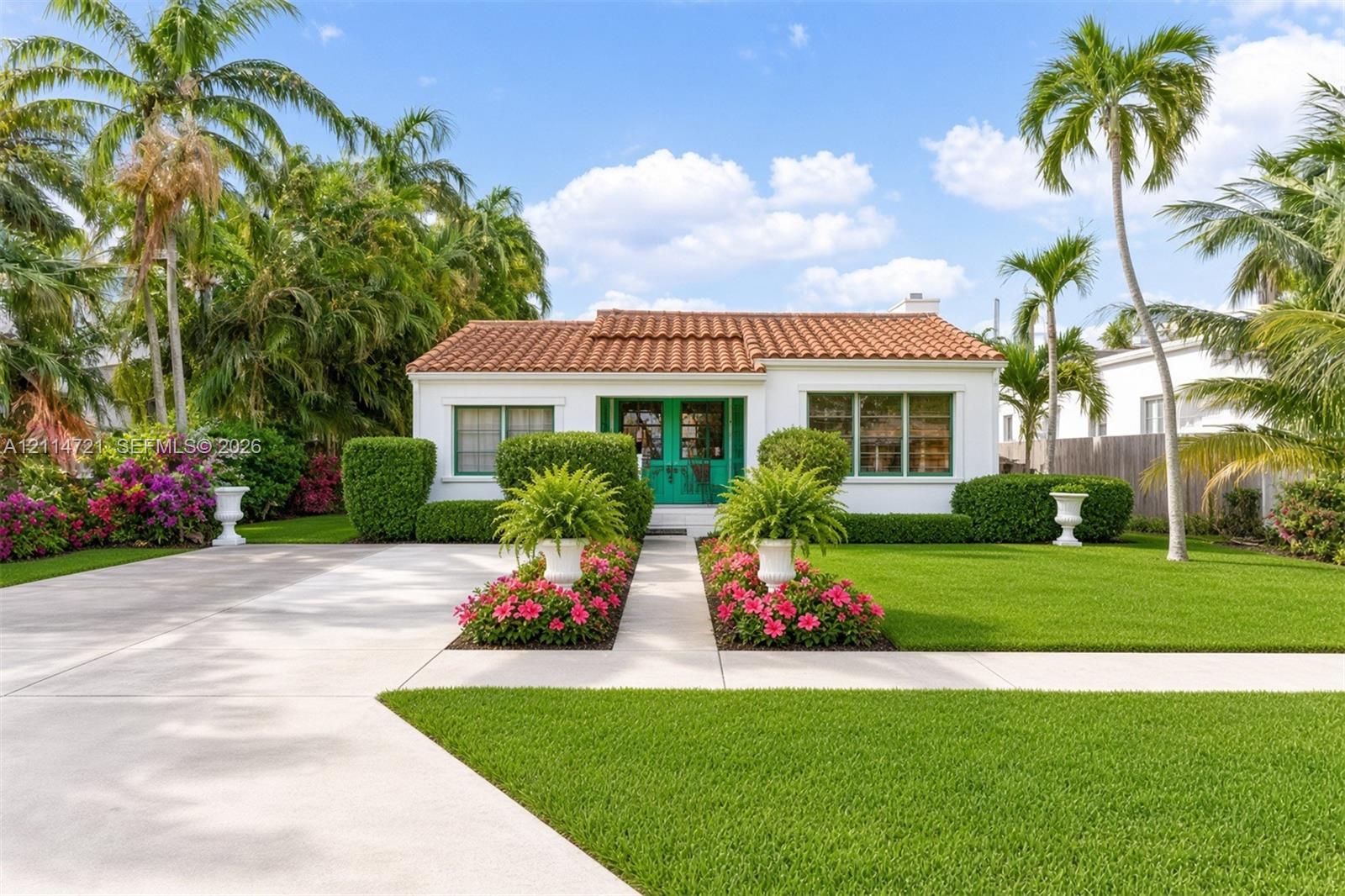Single-story exterior featuring a terracotta tile roof, white stucco facade, teal-framed glass entry doors, and mature palm trees Single-story exterior featuring a terracotta tile roof, white stucco facade, teal-framed glass entry doors, and mature palm trees