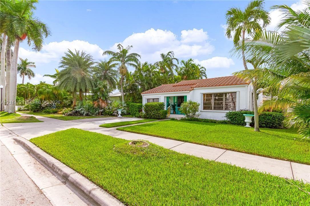 Exterior facade featuring a white stucco finish, a terra cotta tile roof, large paneled windows, and a manicured lawn with mature palm trees