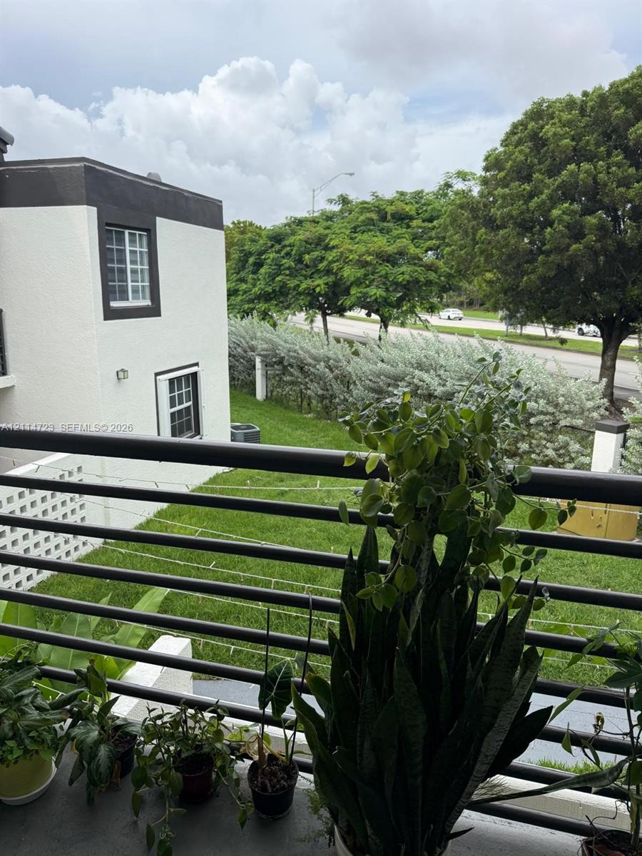 Balcony with black metal railing overlooking a lawn, mature trees, and landscaping