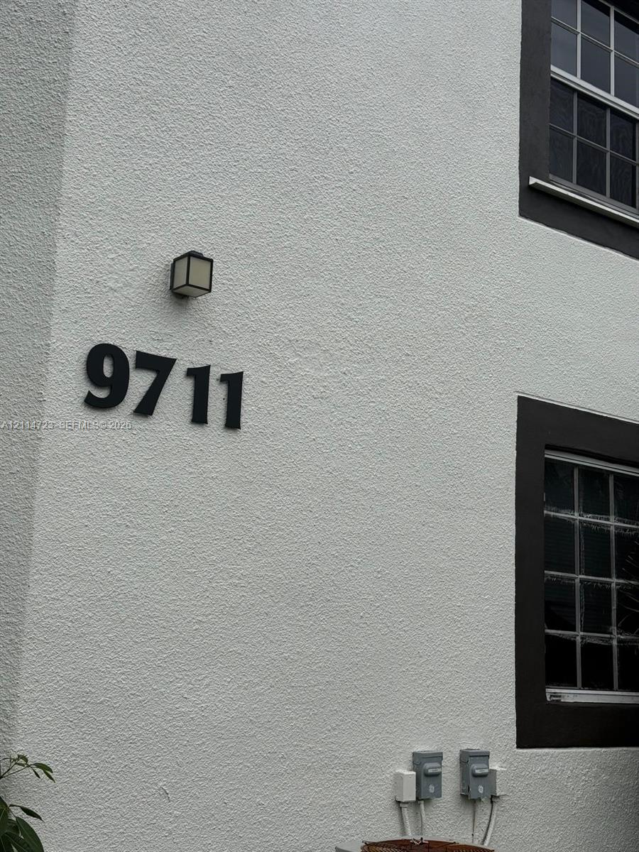 Stucco exterior featuring dark-trimmed multi-pane windows, wall-mounted exterior lighting, and dimensional house numbering