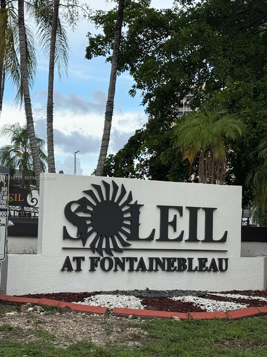 Monolithic white textured monument signage with dimensional black lettering and sun-motif graphic, set against a backdrop of mature palm trees and landscaped garden beds with stone mulch borders Monolithic white textured monument signage with dimensional black lettering and sun-motif graphic, set against a backdrop of mature palm trees and landscaped garden beds with stone mulch borders