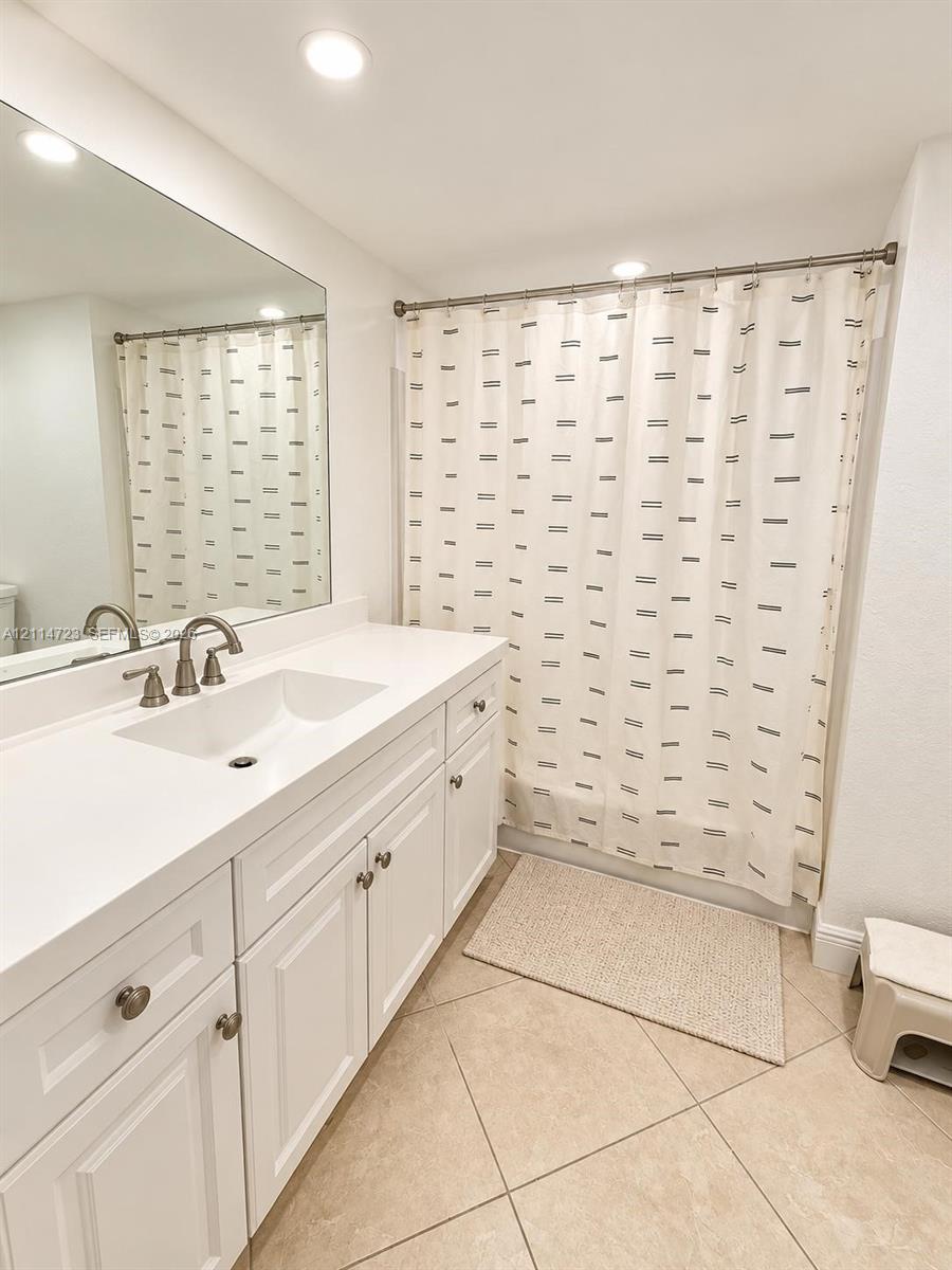 White cabinetry vanity featuring a rectangular integrated sink, white countertop, brushed metal faucet, and full-width wall mirror, complemented by tile flooring White cabinetry vanity featuring a rectangular integrated sink, white countertop, brushed metal faucet, and full-width wall mirror, complemented by tile flooring