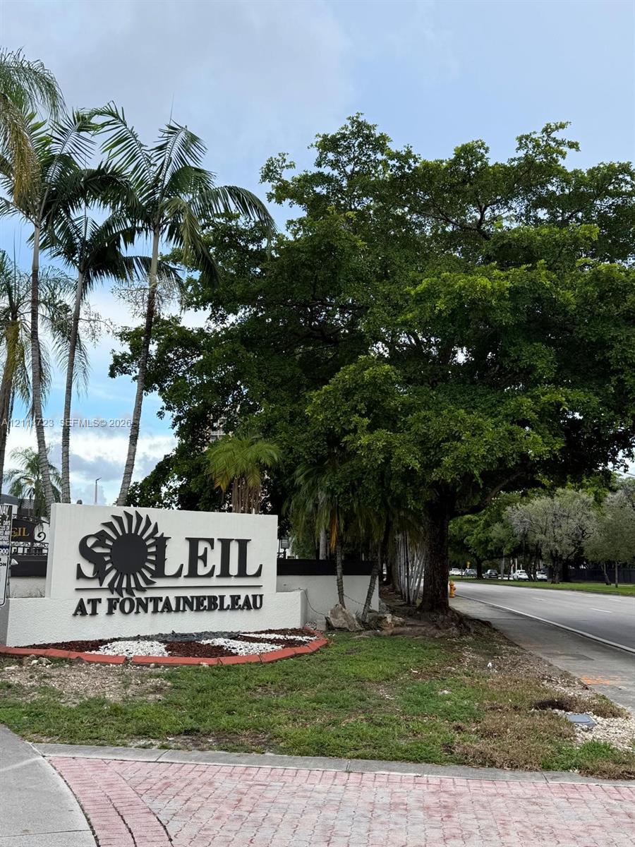 Community monument sign featuring dimensional lettering, decorative landscaping with ground cover, and mature palm and hardwood trees