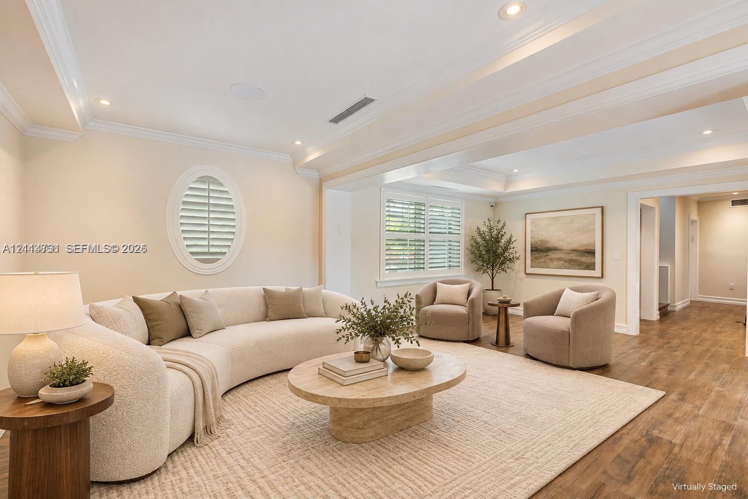 Tray ceilings with recessed lighting, oval accent window with plantation shutters, and wood-finish flooring