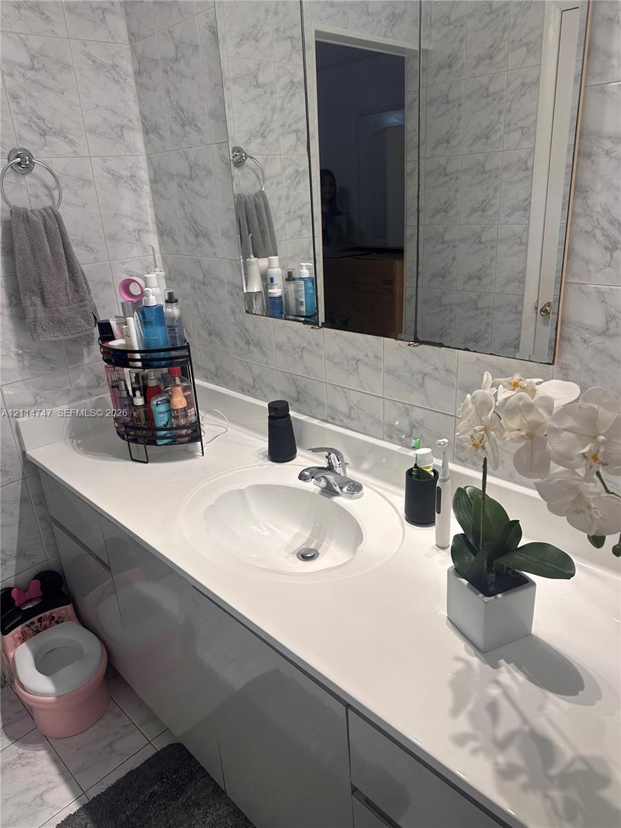 Bathroom vanity featuring a solid-surface countertop with an integrated oval sink, chrome faucet, mirrored medicine cabinet, and wall-to-wall light-toned tiling