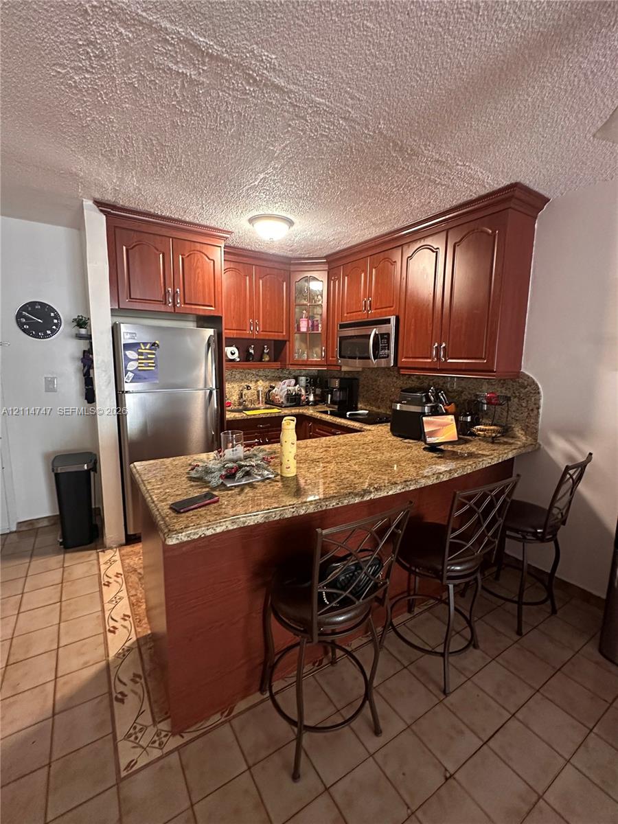 Kitchen featuring raised-panel wood cabinetry, natural stone countertops, integrated breakfast bar, and stainless steel built-in microwave