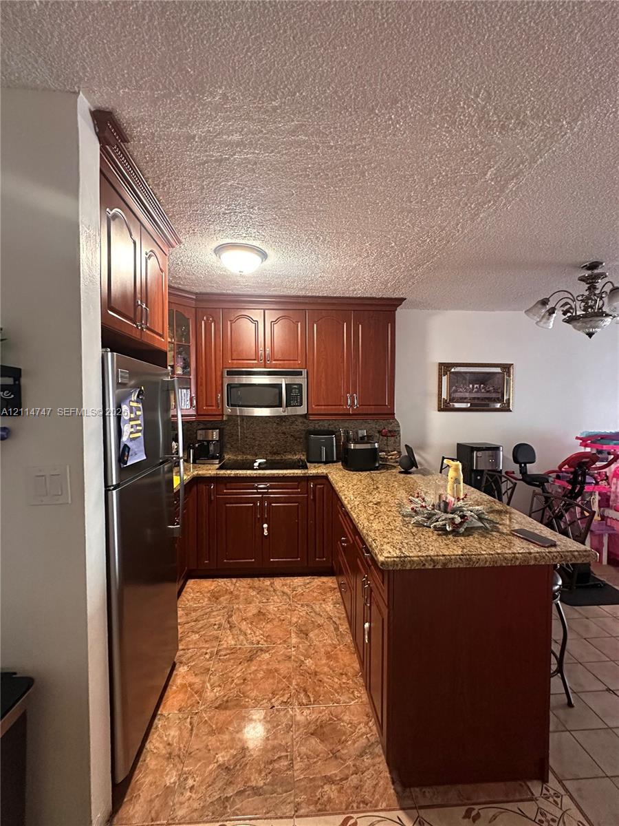 Kitchen featuring stained wood cabinetry, stone-surface countertops, tile flooring, and integrated stainless steel appliances