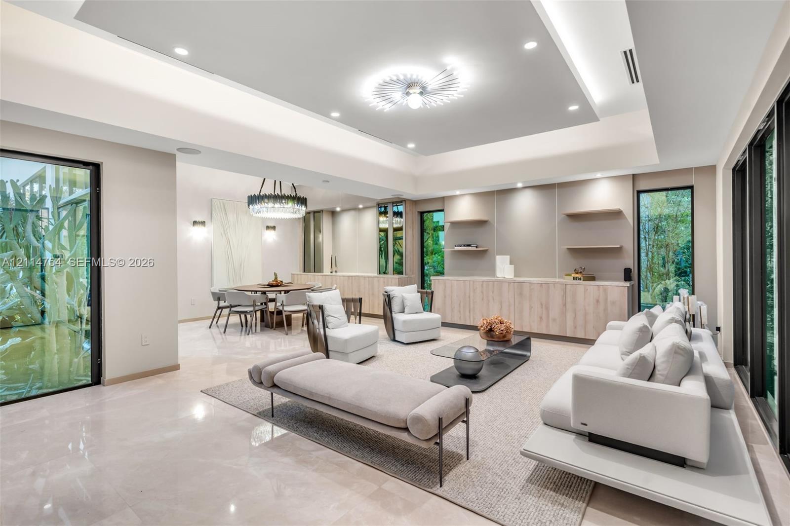 Tray ceiling with recessed lighting, integrated wood-finish cabinetry with stone countertop, floating wall shelves, large-format tile flooring, and floor-to-ceiling glass sliding doors