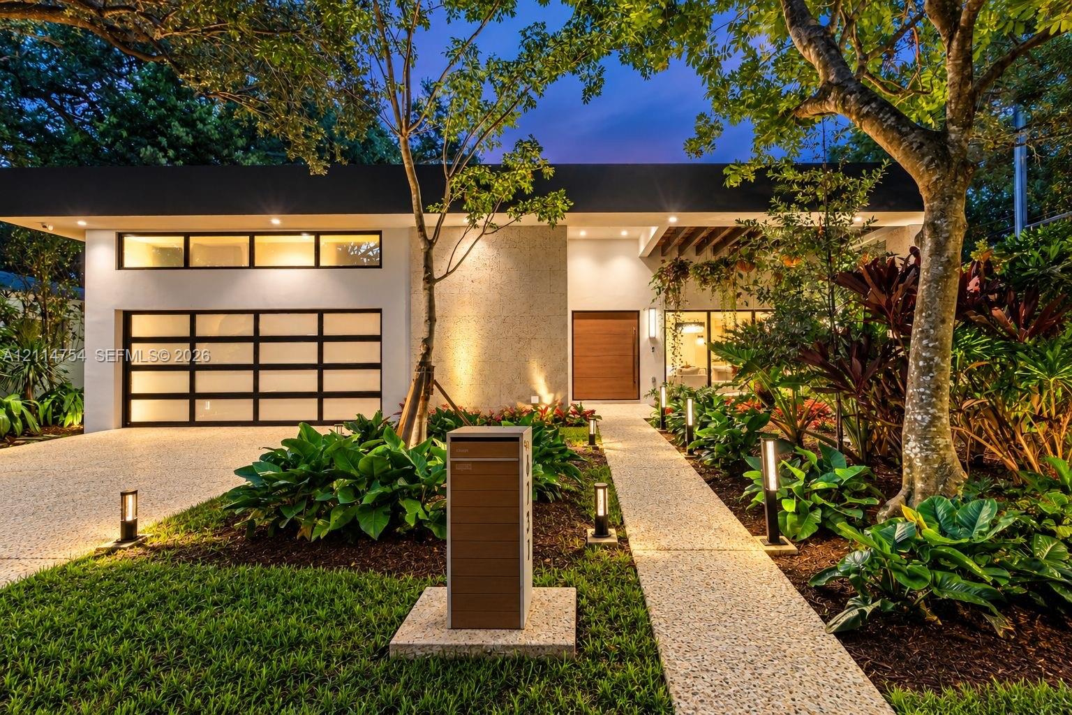 Modern single-story exterior featuring a smooth stucco facade, sectional frosted glass garage door, textured stone accent wall, wood-finish entry door, and exposed timber ceiling beams