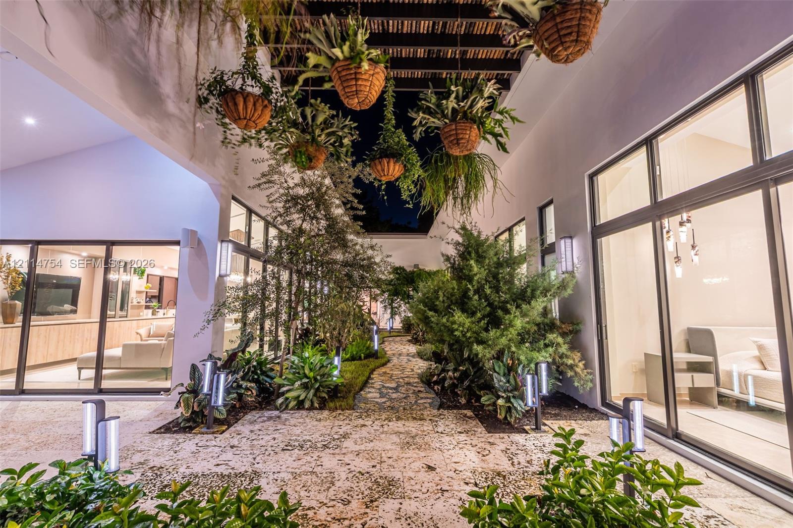 Outdoor area featuring a tiled pool and spa with built-in lighting, expansive stone-finish patio, and mature perimeter landscaping